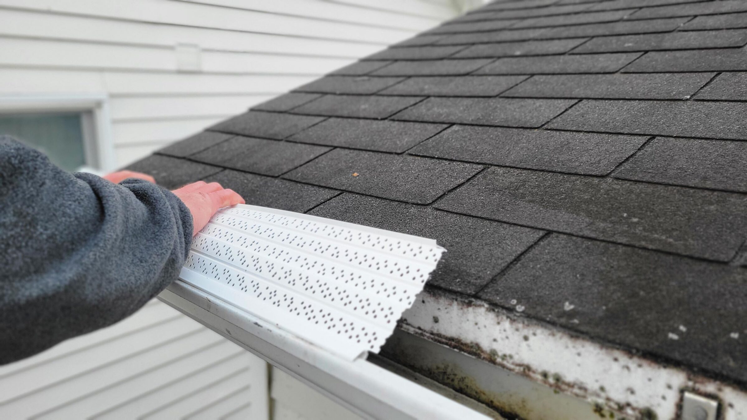 hands of person installing micro mesh gutter guard to house gutters